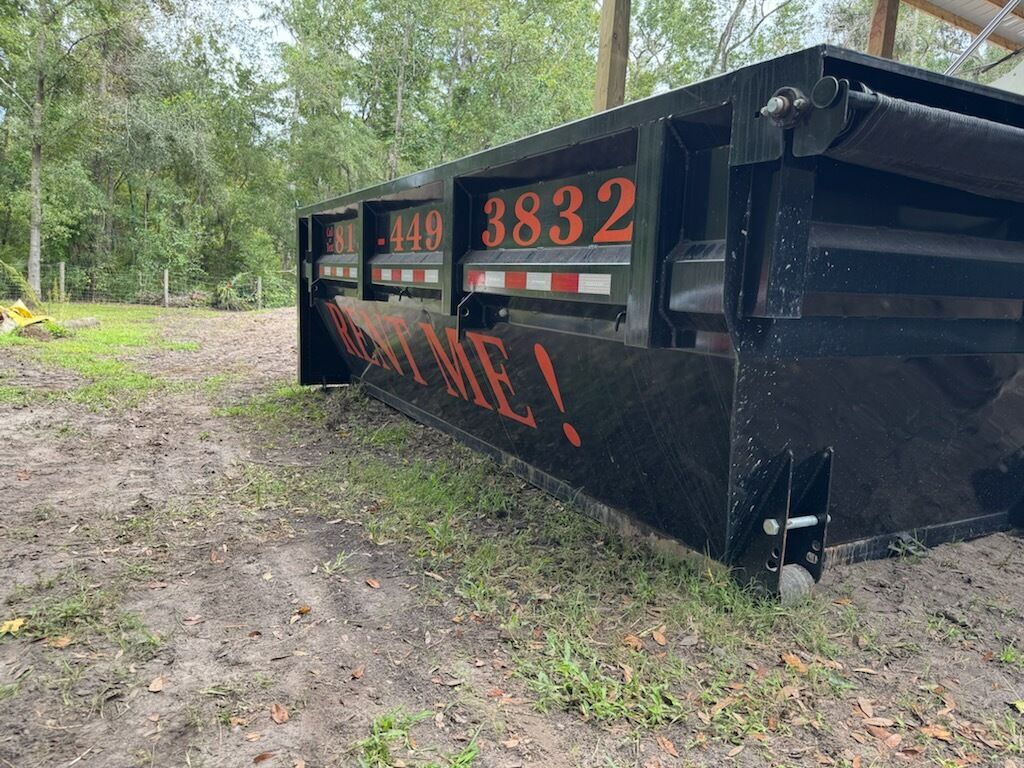 Black dumpster with orange lettering, sitting on dirt and grass.