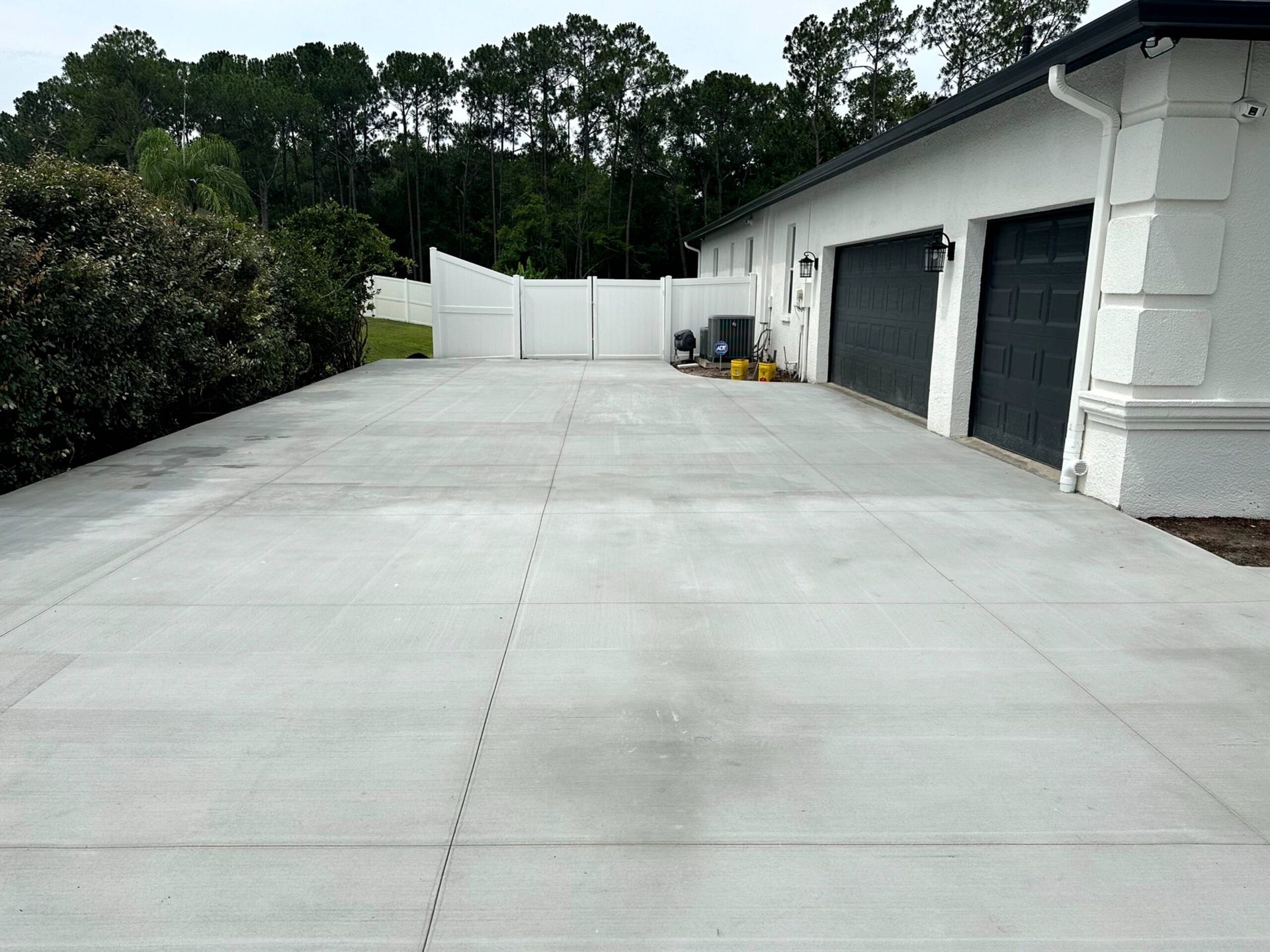 Gray concrete driveway leading to a white house with black garage doors.