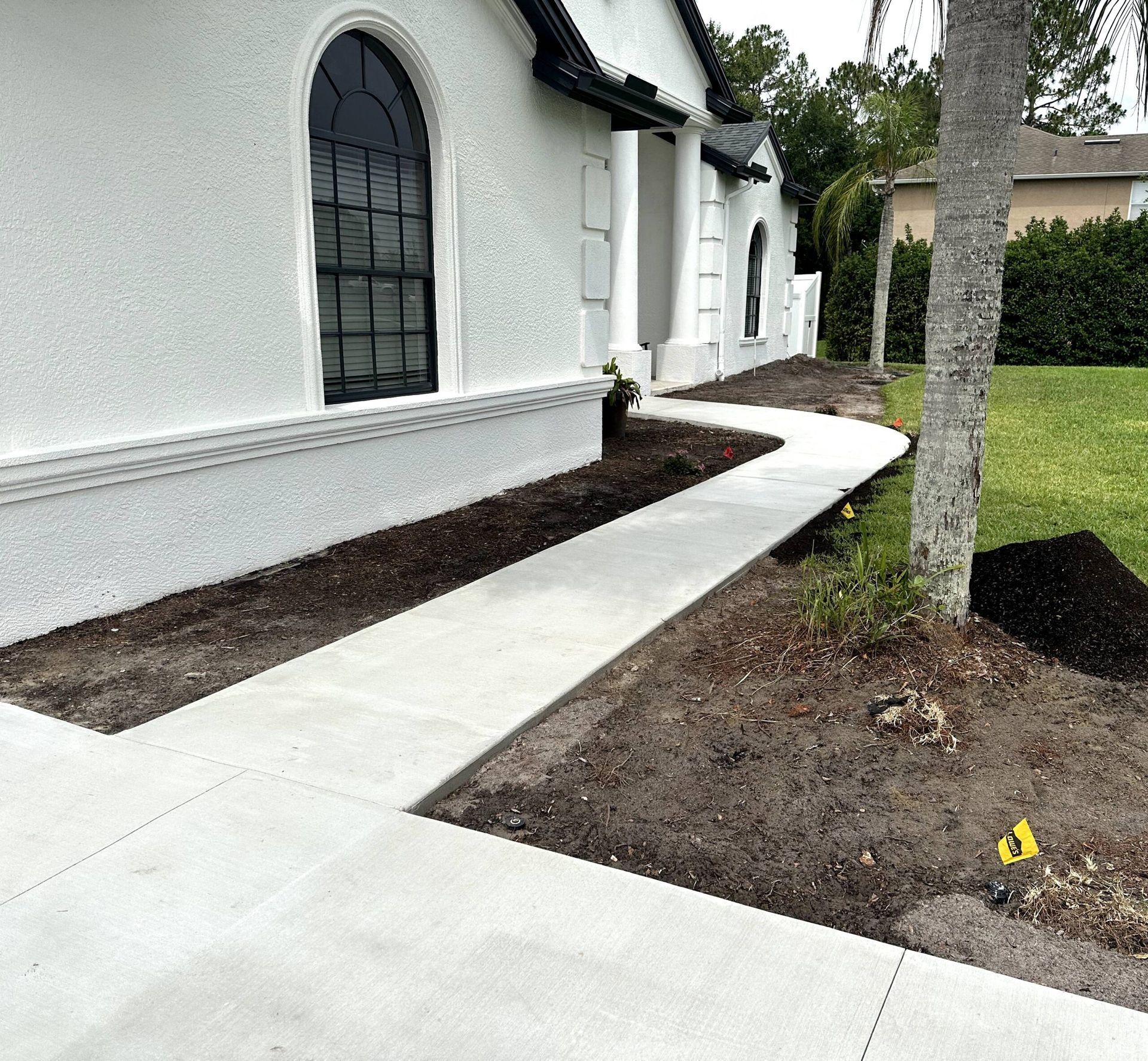 Concrete walkway leading to a white house with black trim and a large arched window.