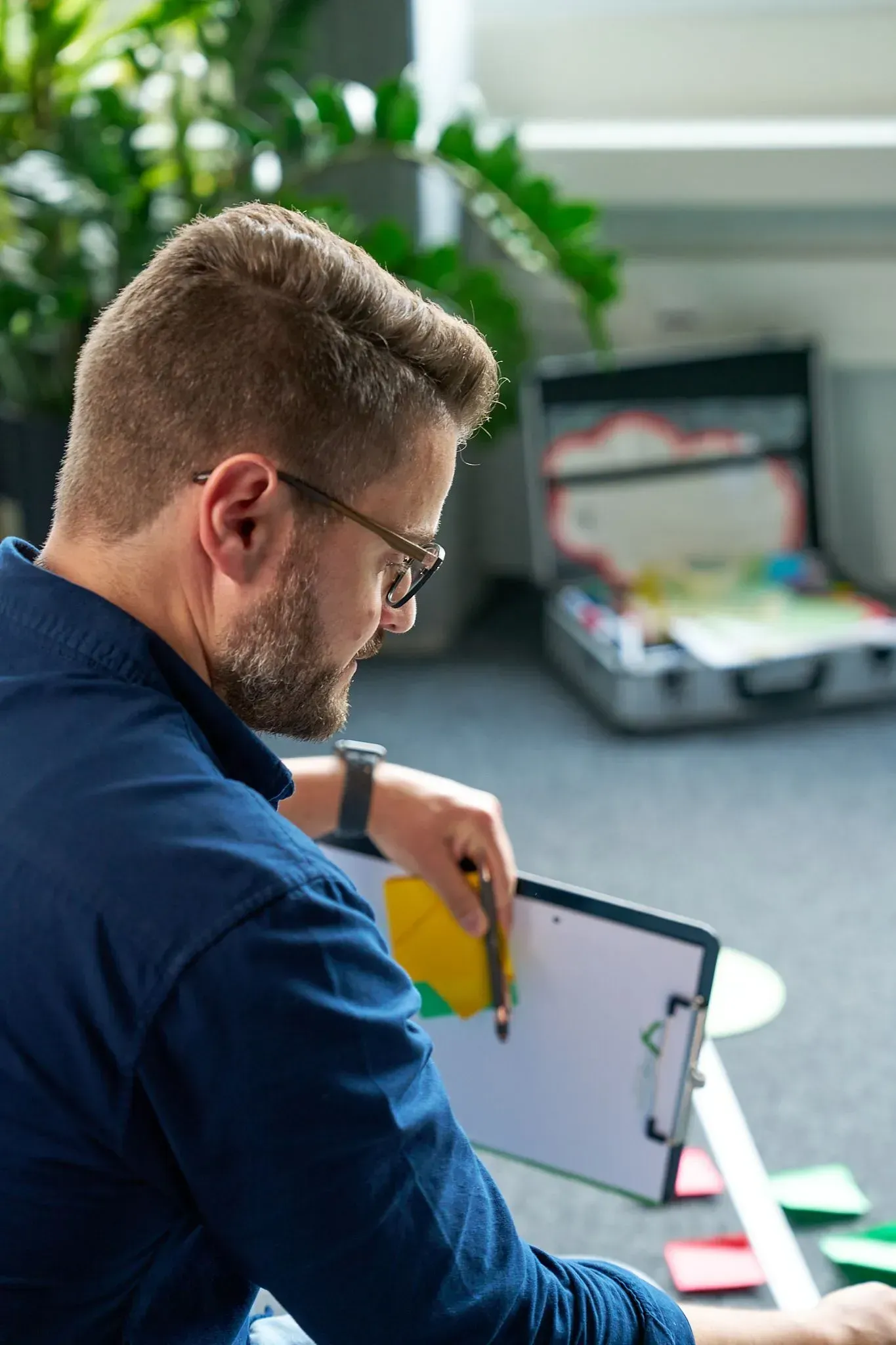 Eine Person benutzt einen Laptop an einem Schreibtisch in einem hellen Büro; daneben steht ein geöffneter Koffer.
