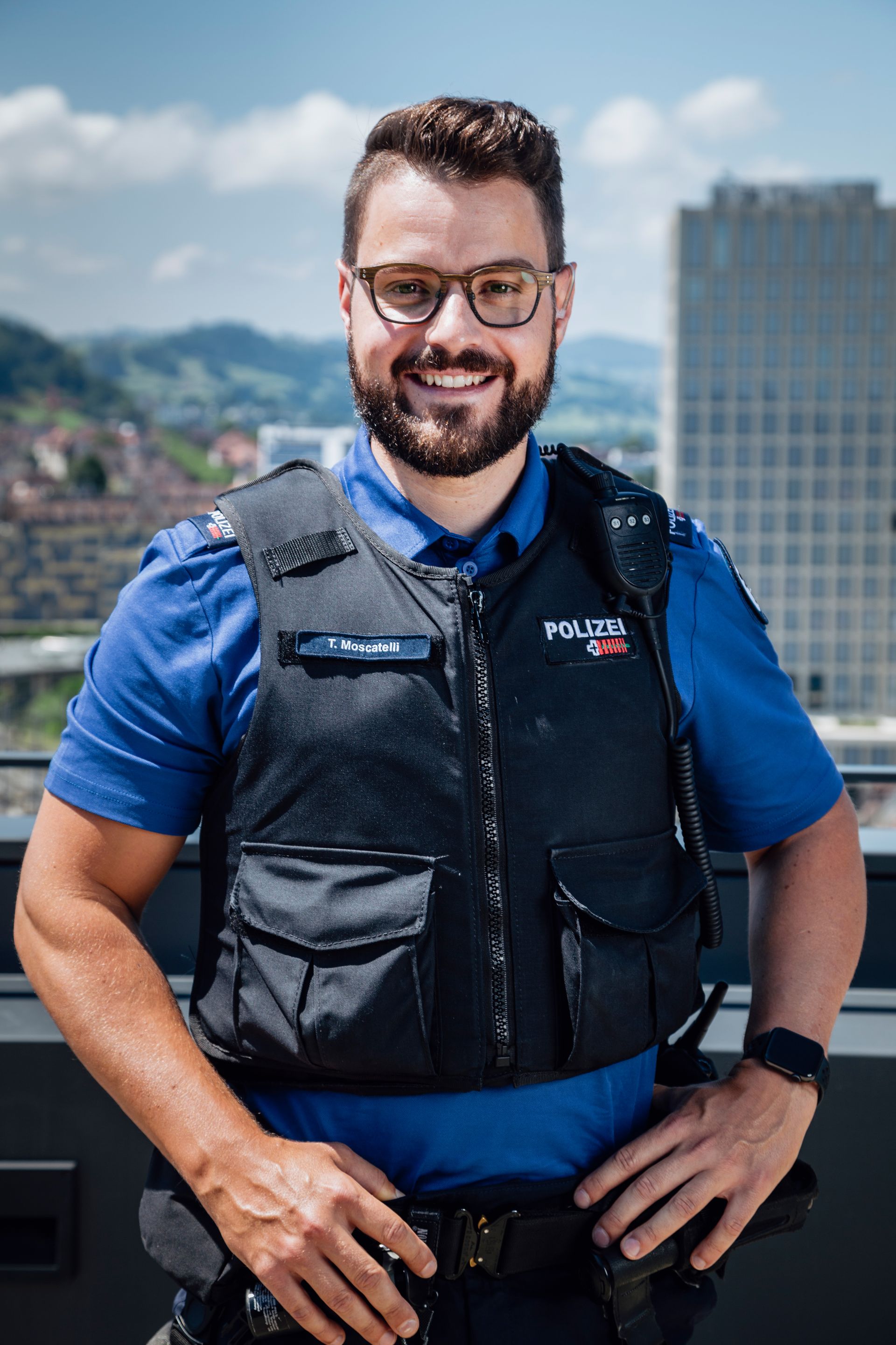 Thomas in Polizei Uniform steht im Freien vor dem Hintergrund von Stadtgebäuden.