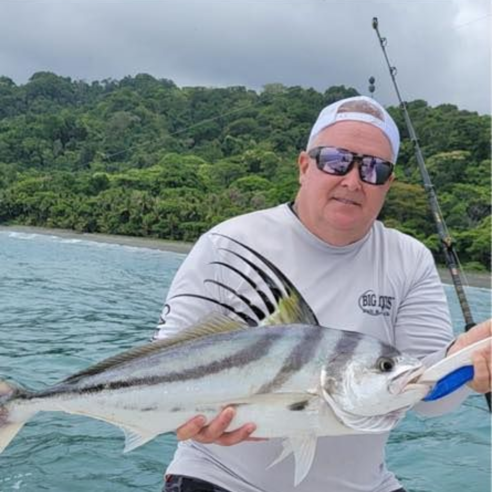 Man on boat holding a fish, with water and trees in the background.
