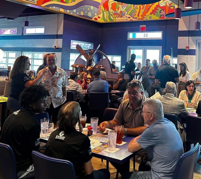 People gathered in a brightly-colored restaurant, some seated at tables, others standing and talking.