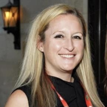Blonde woman smiling, wearing a black top, standing indoors.