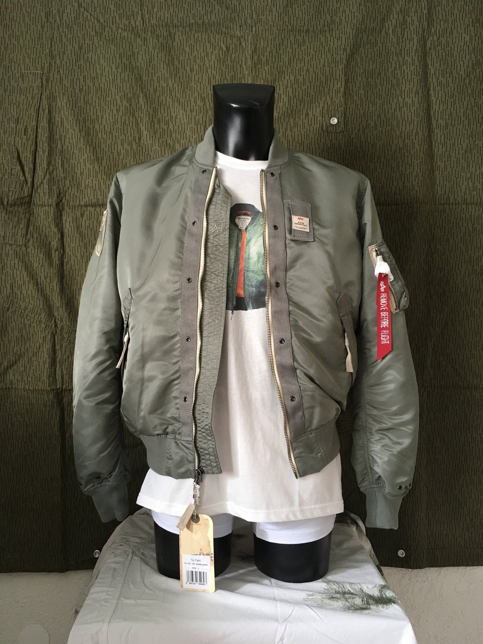 Eine grüne Bomberjacke im Militärstil, die auf einer Schaufensterpuppe über einem weißen T-Shirt präsentiert wird.