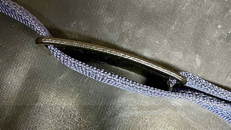 Blaue geflochtene Kordel, die durch eine dunkle, gebogene Metallschlaufe gefädelt ist.