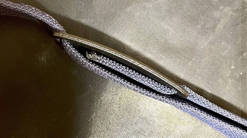 Nahaufnahme einer silberfarbenen Metallschnalle an einer hellvioletten und schwarzen gewebten Kordel.