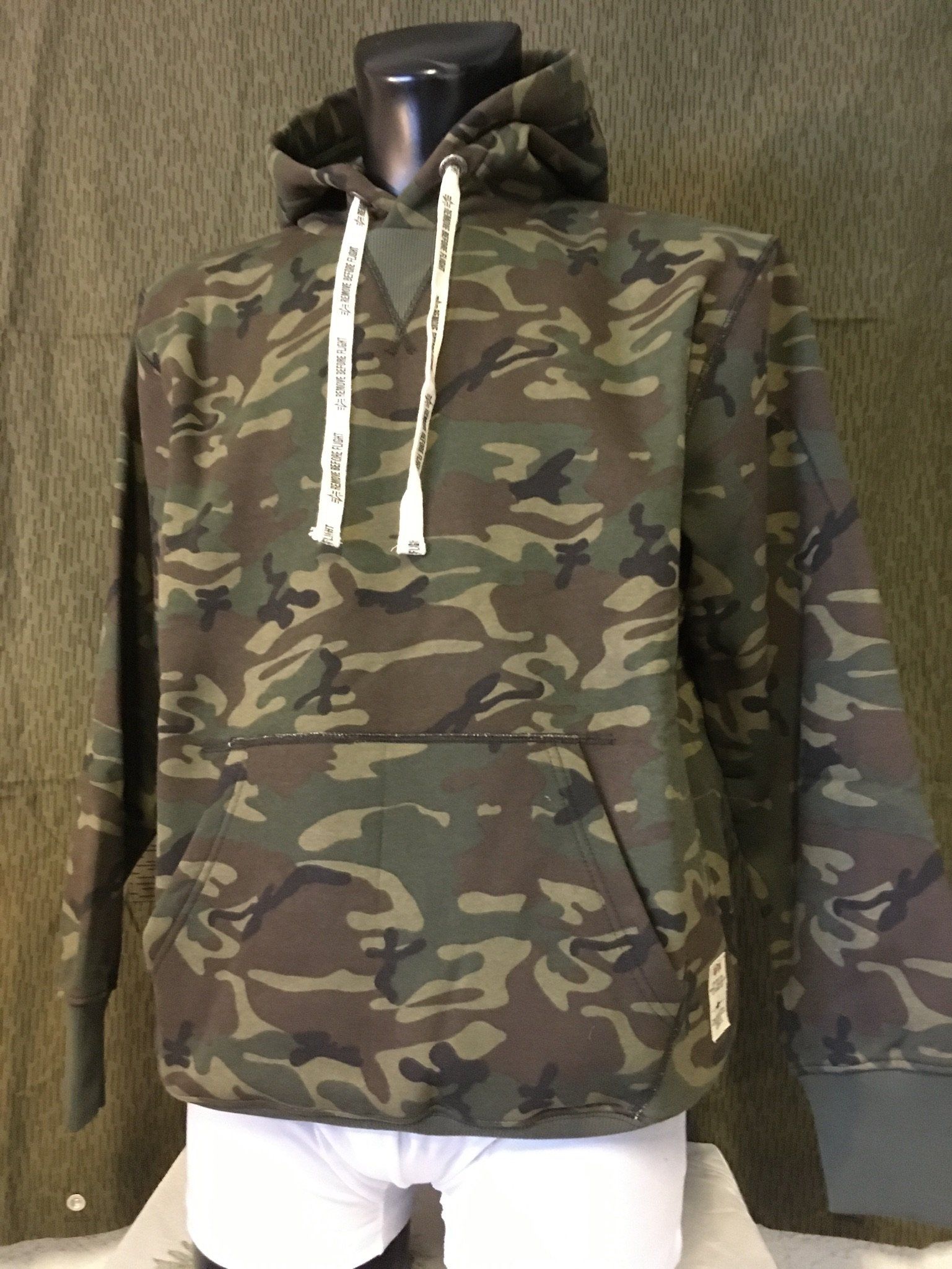 Camouflage-Kapuzenpullover an einer Schaufensterpuppe; Vordertasche, Kordelzug, grün-braunes Muster.