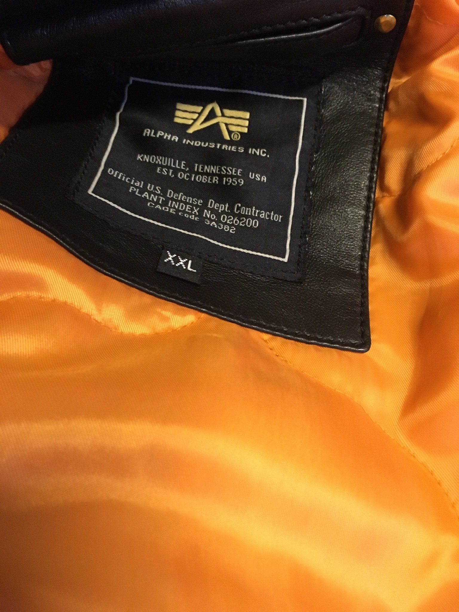 Schwarzes Jackenetikett aus Leder von Alpha Industries mit weißem Text auf orangefarbenem Futter. Größe: XXL.