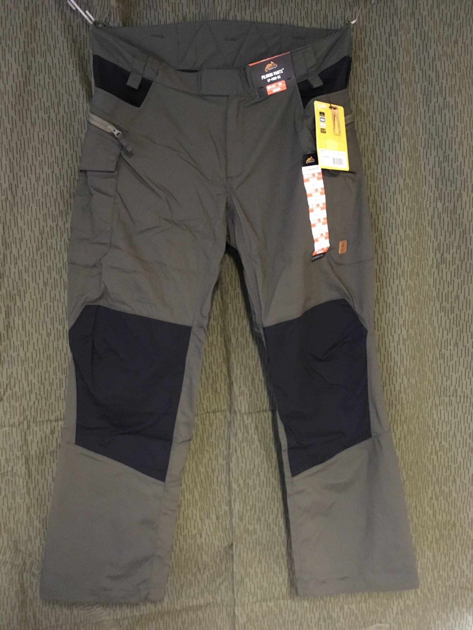 Graue und schwarze Arbeitshosen mit Knieflicken und Cargotaschen, hängen an einem Ständer.