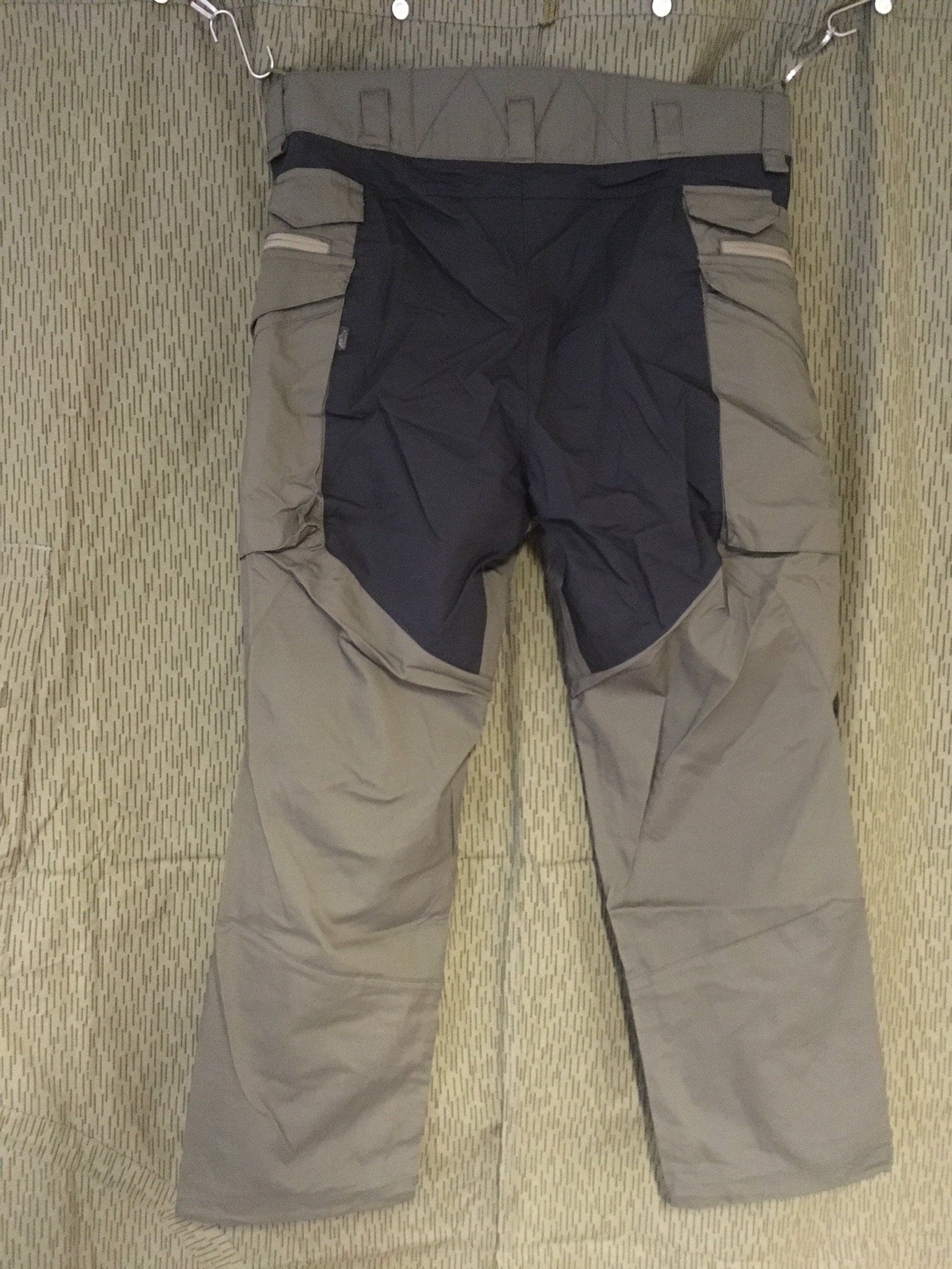 Graue und blaue Skihosen hängen vor einem gemusterten Hintergrund.