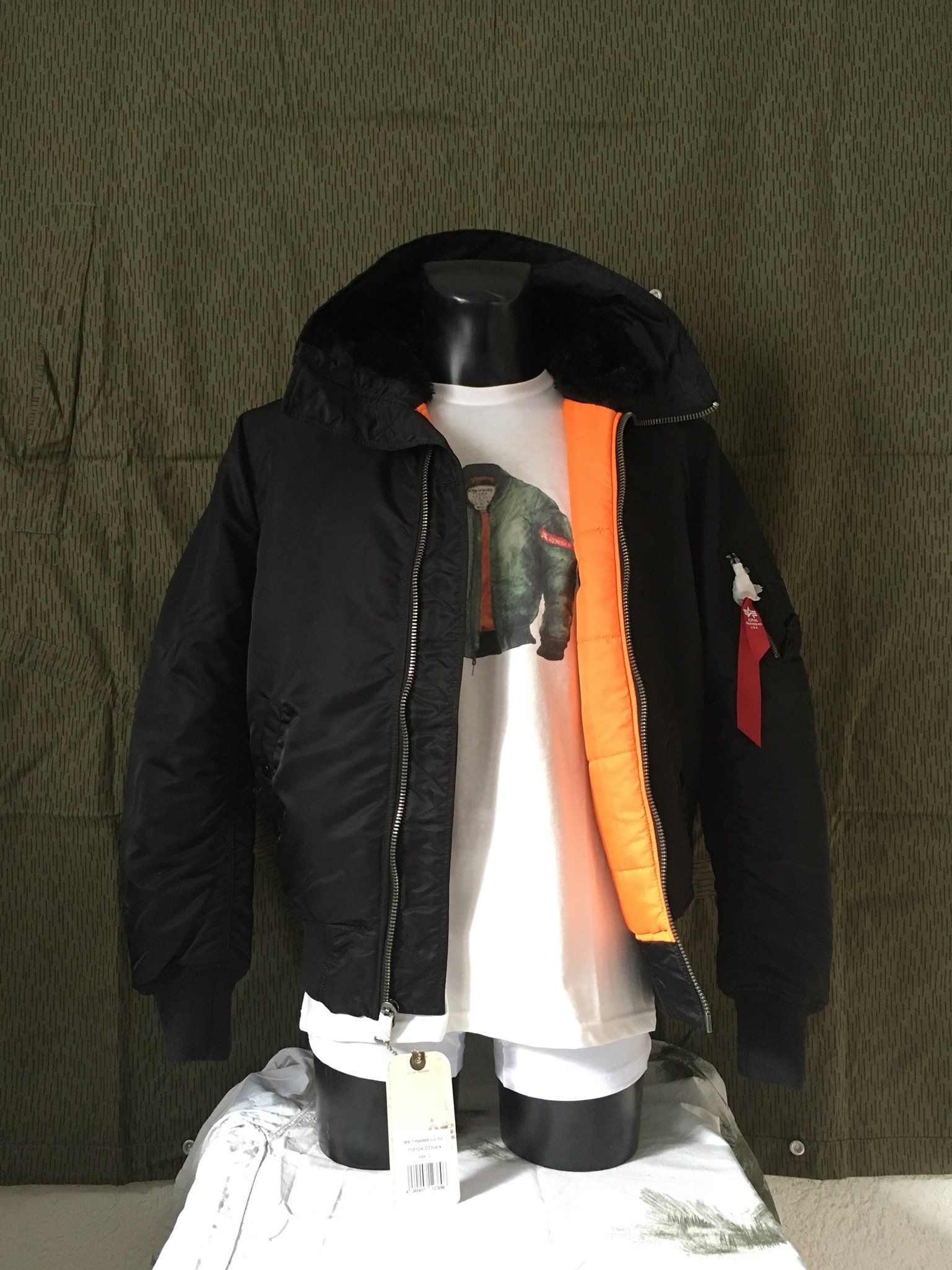 Schwarze Bomberjacke mit orangefarbenem Futter, Kapuze und weißem T-Shirt auf einer Schaufensterpuppe.