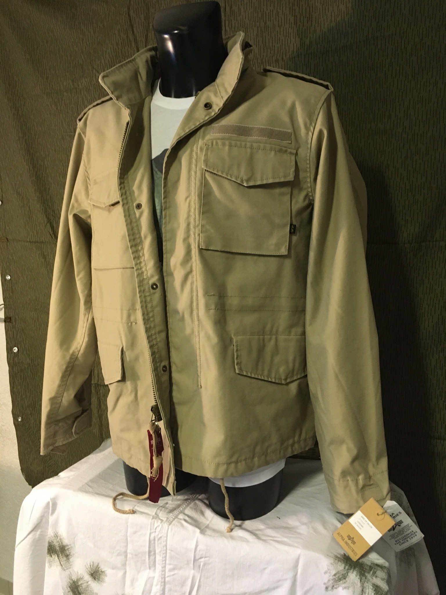 Hellbraune Jacke an einer Schaufensterpuppe, darunter ein weißes Hemd. Beigefarbene Fassung mit einem Etikett.