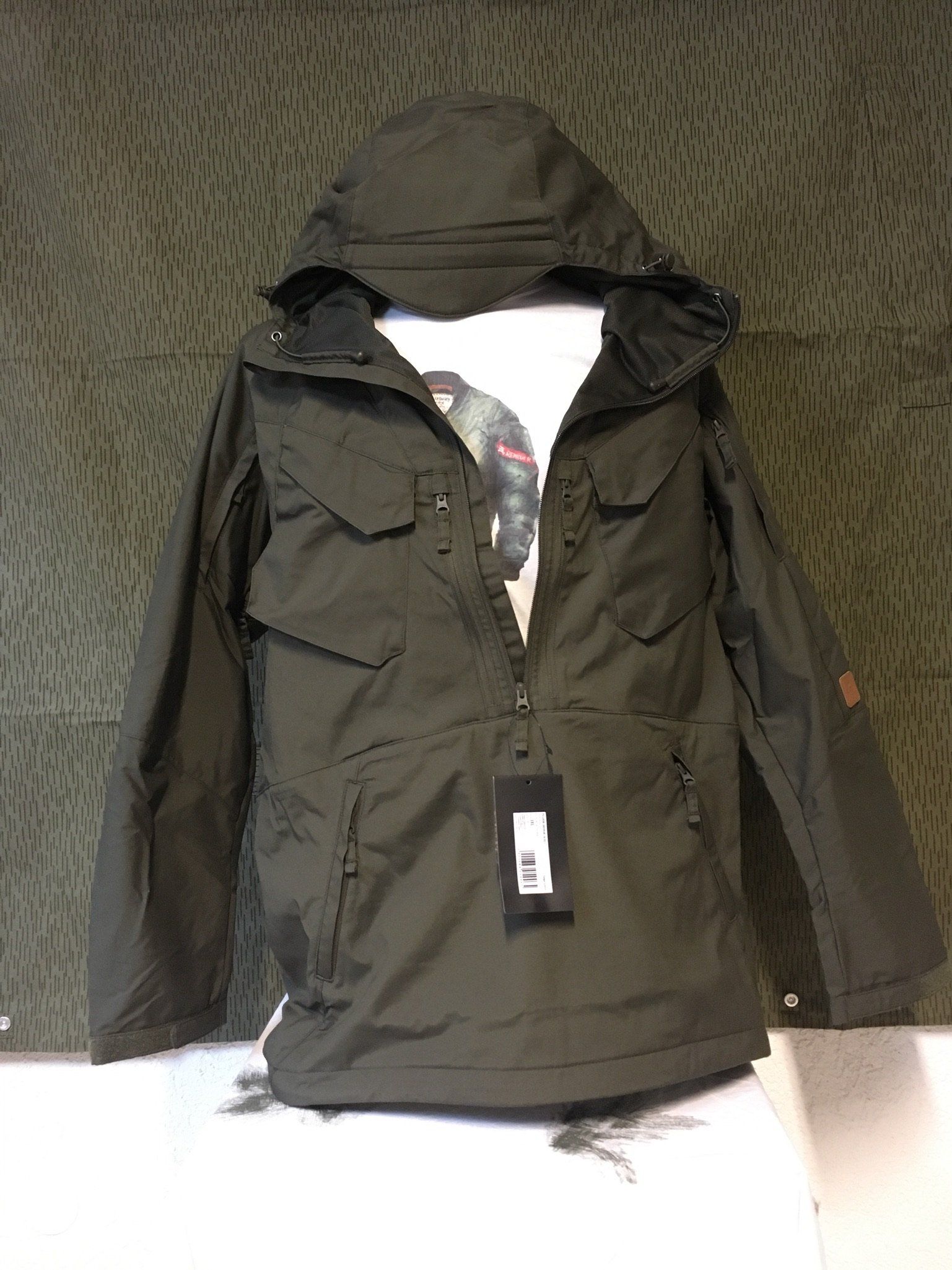 Dunkelgrüner Anorak mit Kapuze, Vordertaschen und Etikett.