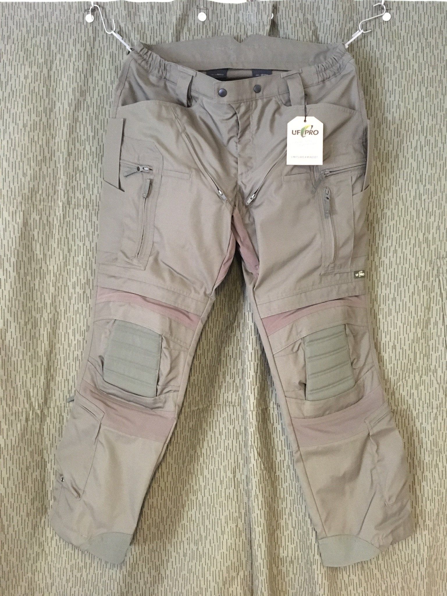 Hellbraune Cargohose mit geflickten Knien und Etikett, das an einem Kleiderbügel hängt.