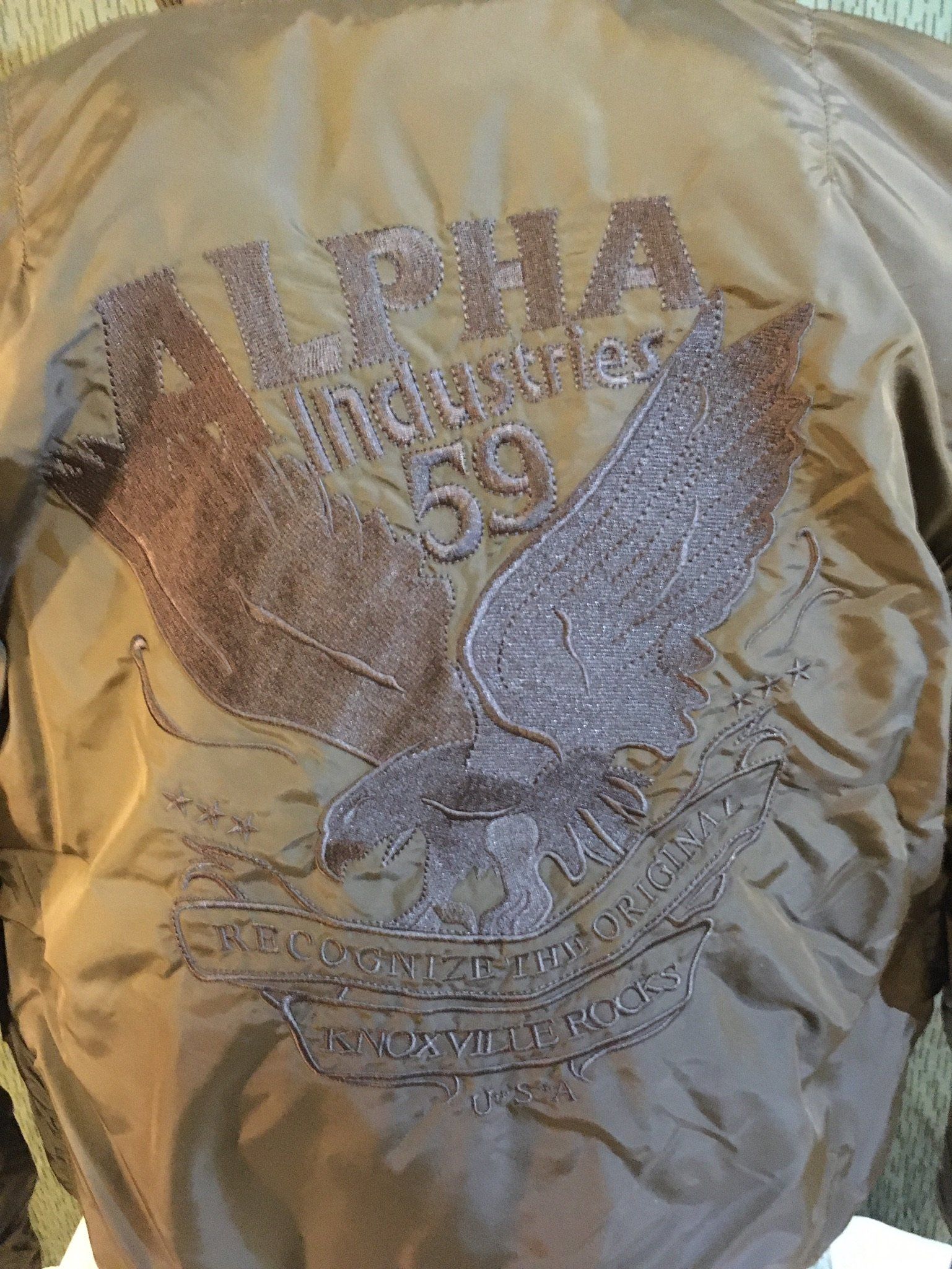 Olivgrüne Jackenrückseite von Alpha Industries, bestickt mit „ALPHA Industries '69“ und einem Adlerdesign.
