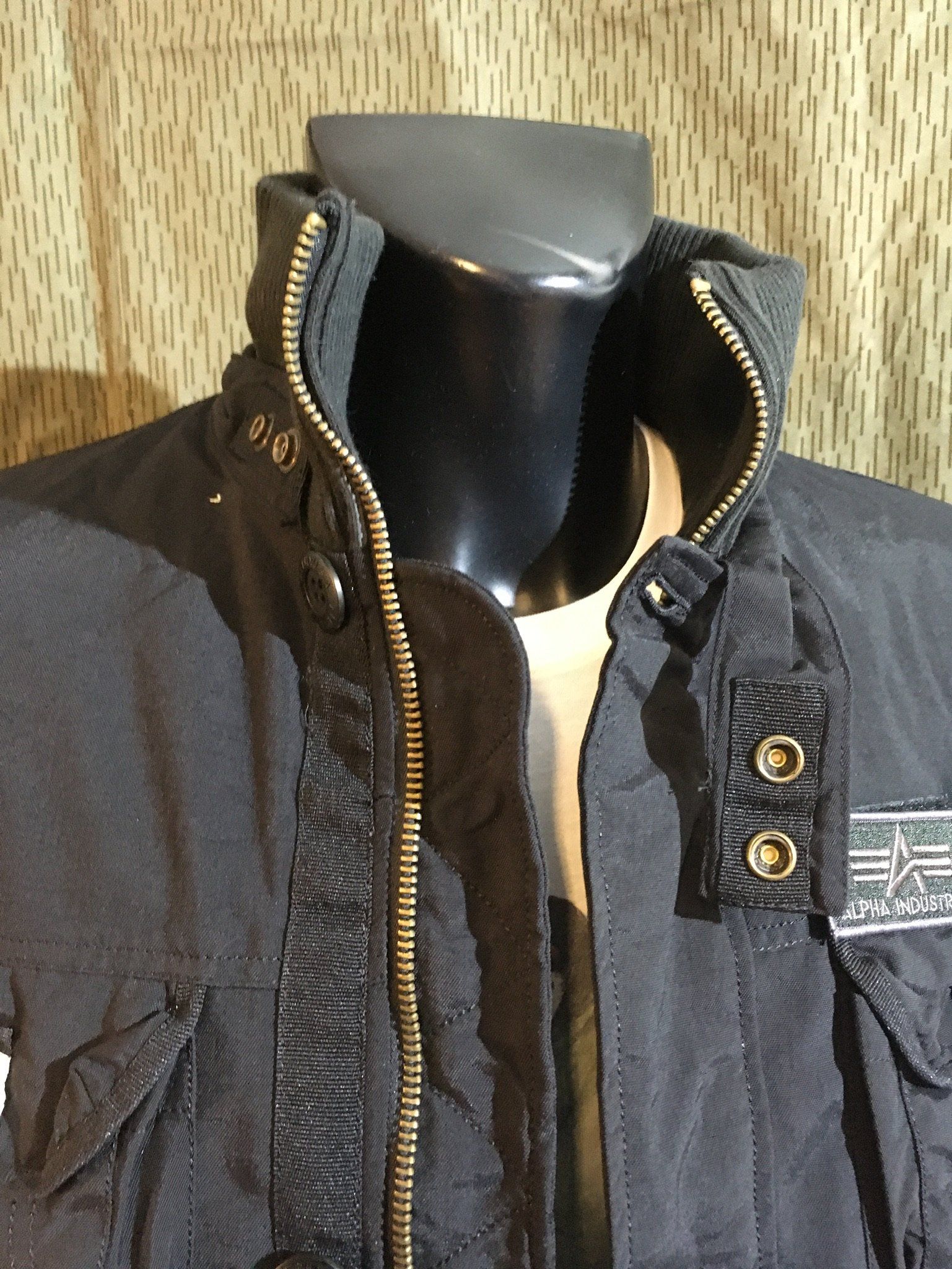 Schwarze Jacke an einer Schaufensterpuppe, mit hohem Kragen und Reißverschluss und einem Patch am Ärmel.