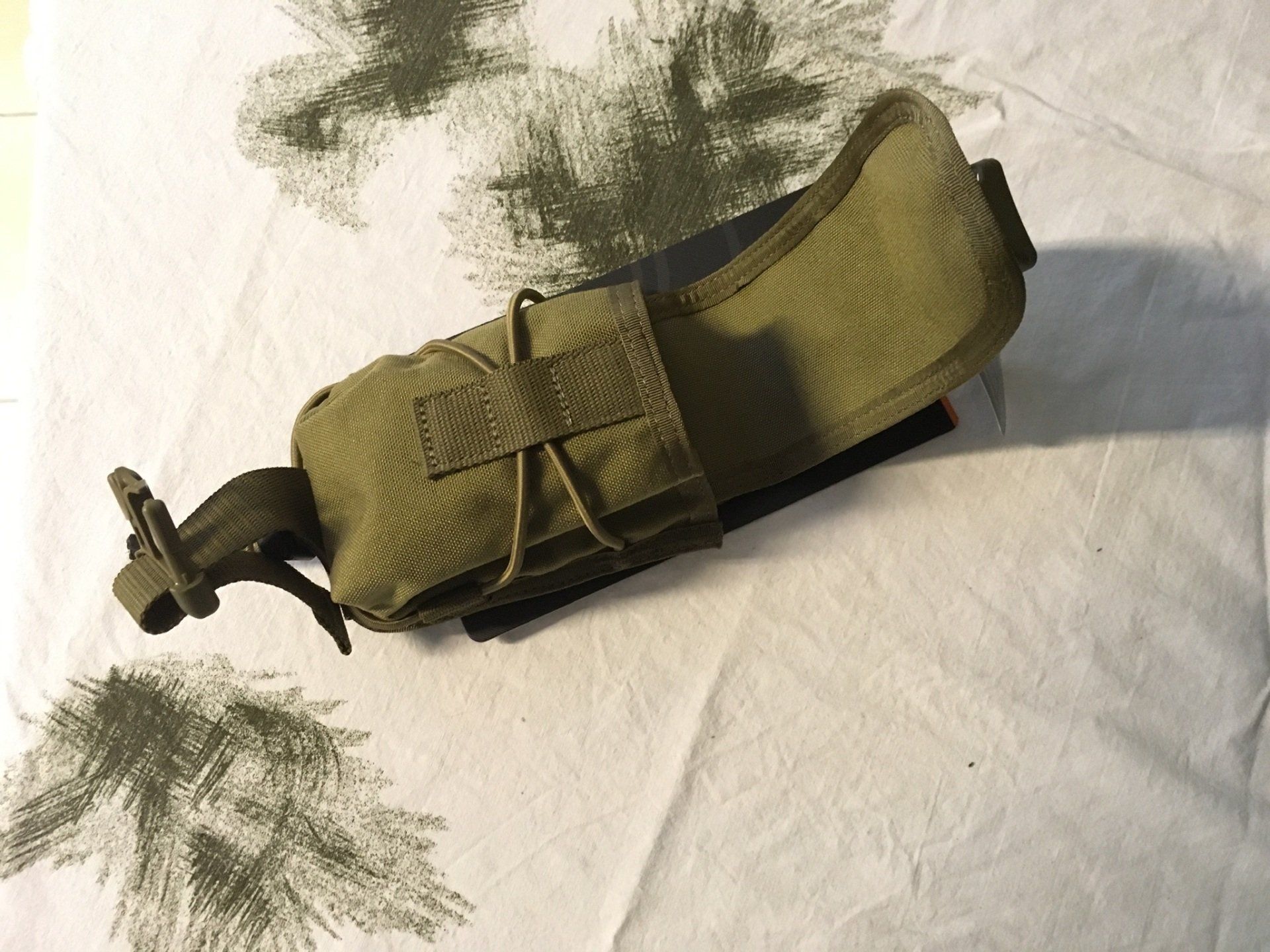 Grüne taktische Tasche auf weiß und grün gemusterter Oberfläche.