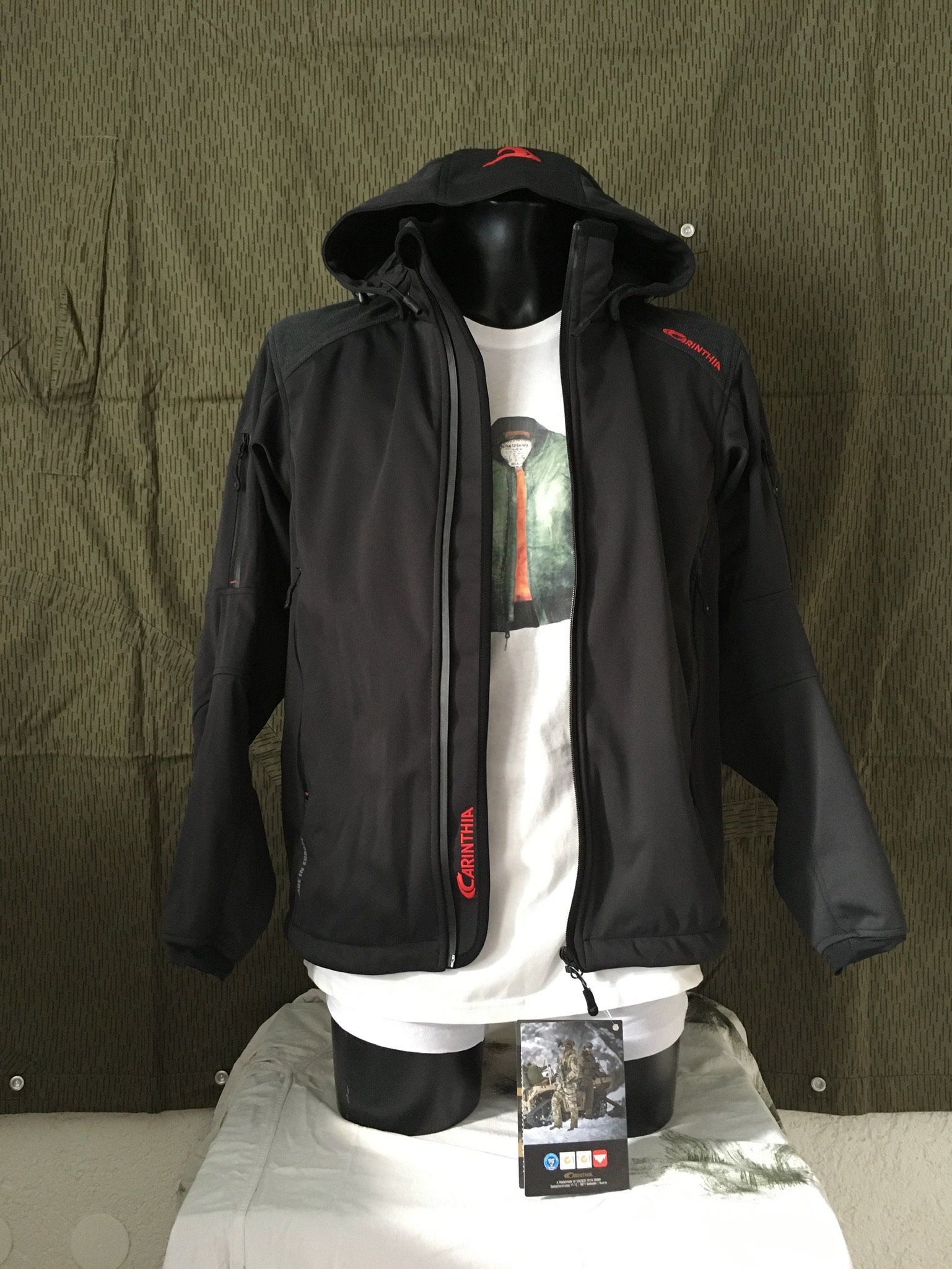 Schwarze Jacke mit Kapuze an einer Schaufensterpuppe, über einem weißen T-Shirt. Die Jacke hat einen roten Schriftzug.