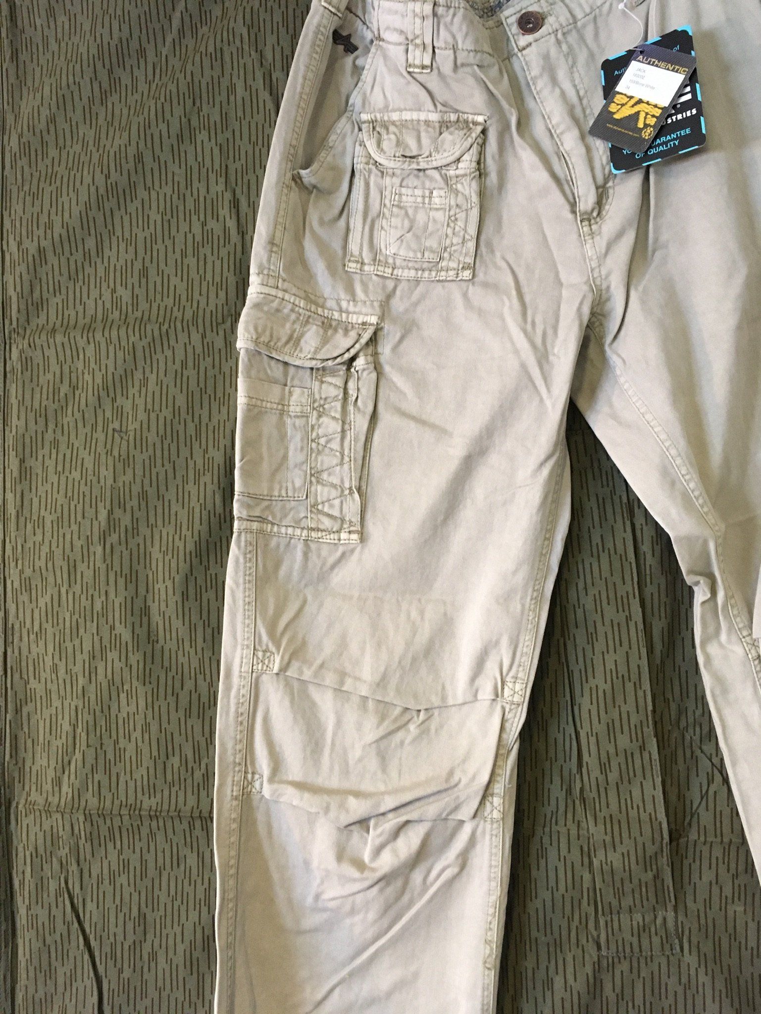 Hellbraune Cargohose mit mehreren Taschen auf Camouflage-Hintergrund.