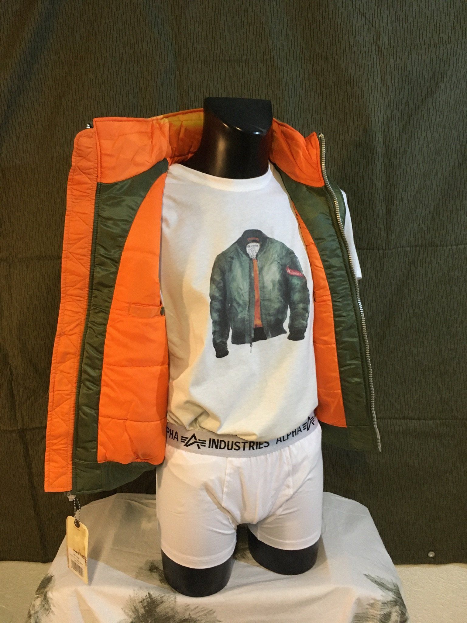 Schaufensterpuppe mit orange-grüner Jacke, Bomberjacke, T-Shirt und weißer Unterhose.