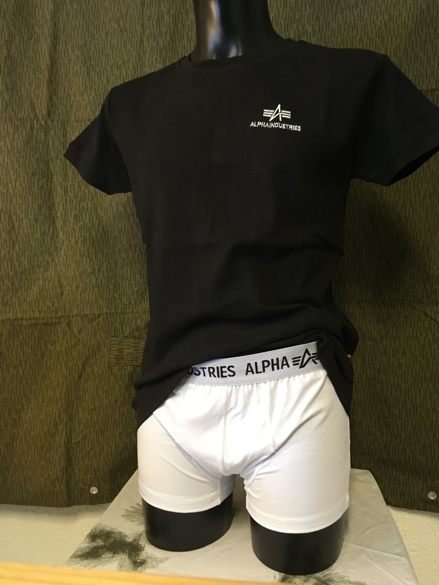 Schwarzes T-Shirt und weiße Boxershorts an einer Schaufensterpuppe. „ALPHA“-Logo auf Shirt und Hosenbund.