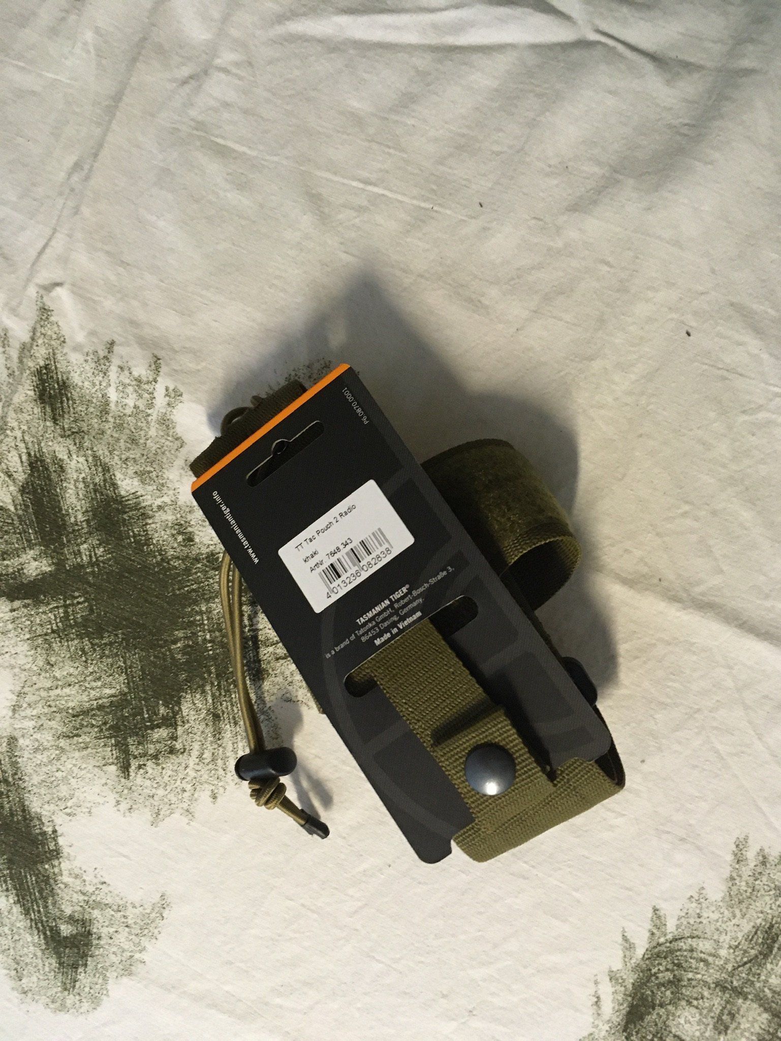 Ein schwarzes Handfunkgerät in einem grünen Holster, das auf einer weiß-grün gemusterten Oberfläche liegt.