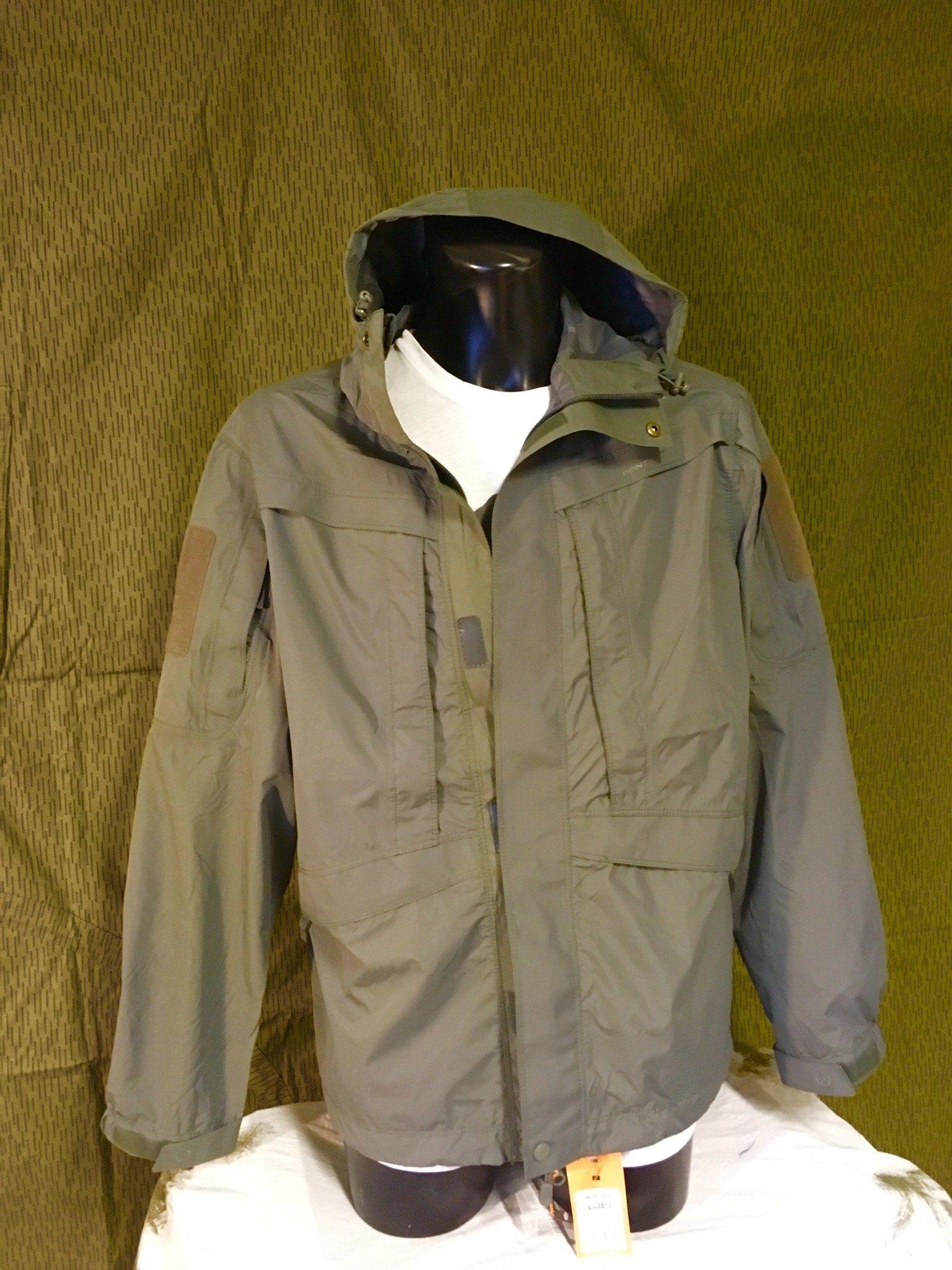 Grüne Jacke im Militärstil mit Kapuze und braunen Aufnähern, ausgestellt auf einer Schaufensterpuppe.