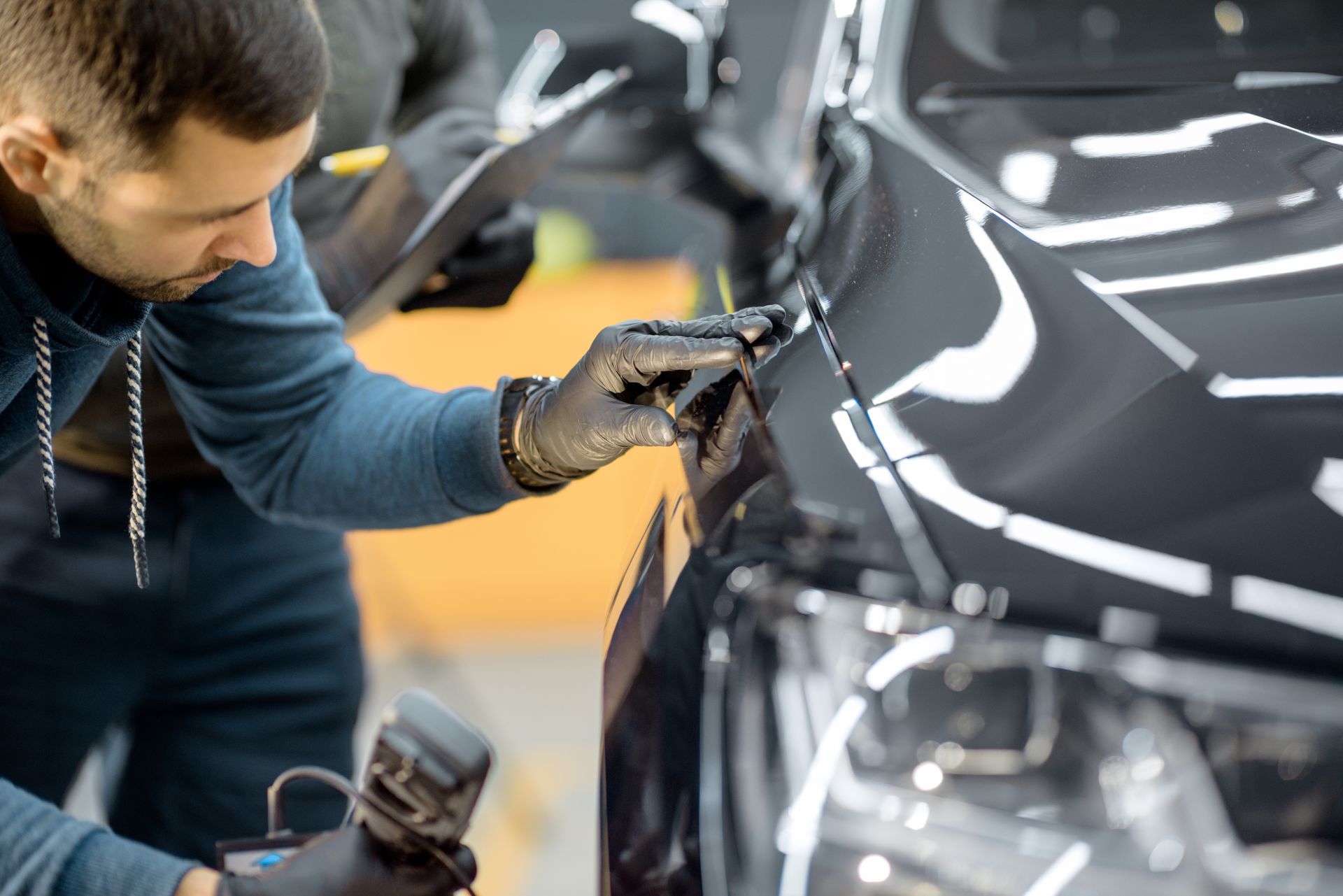A male car service worker examines and wipes the surface of a sleek, black car.