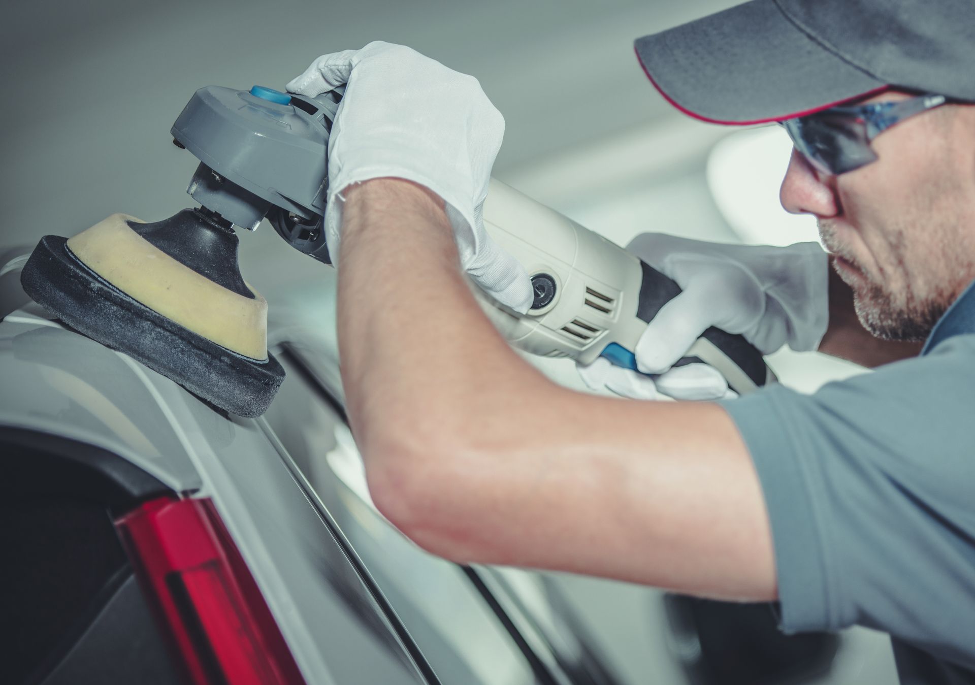 A male collision center worker polishes the exterior of a white car.