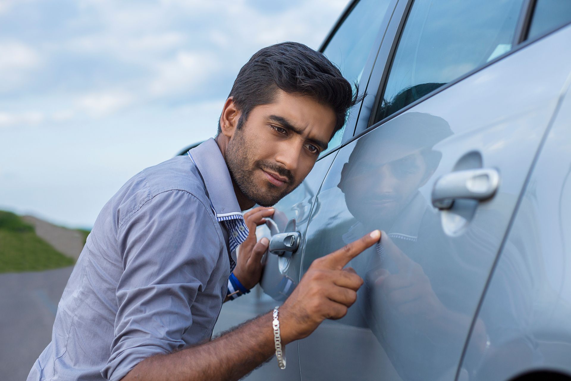 Man pointing at car door scratch, inspecting vehicle damage for insurance or repair assessment.