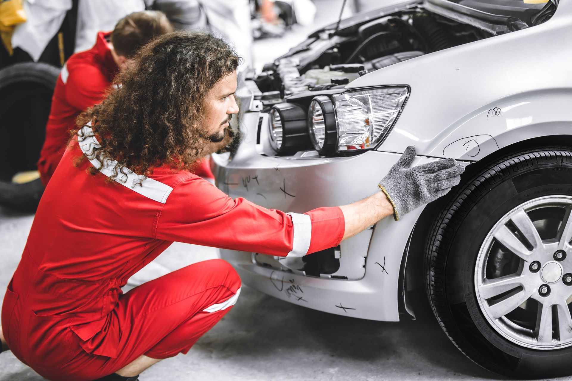 Collision repair experts are fixing a damaged front bumper at the auto workshop after a crash.