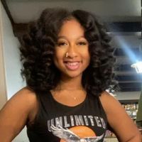 A woman with curly hair is wearing a black tank top and smiling.