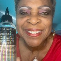 A woman is smiling while holding a bottle of hair product.