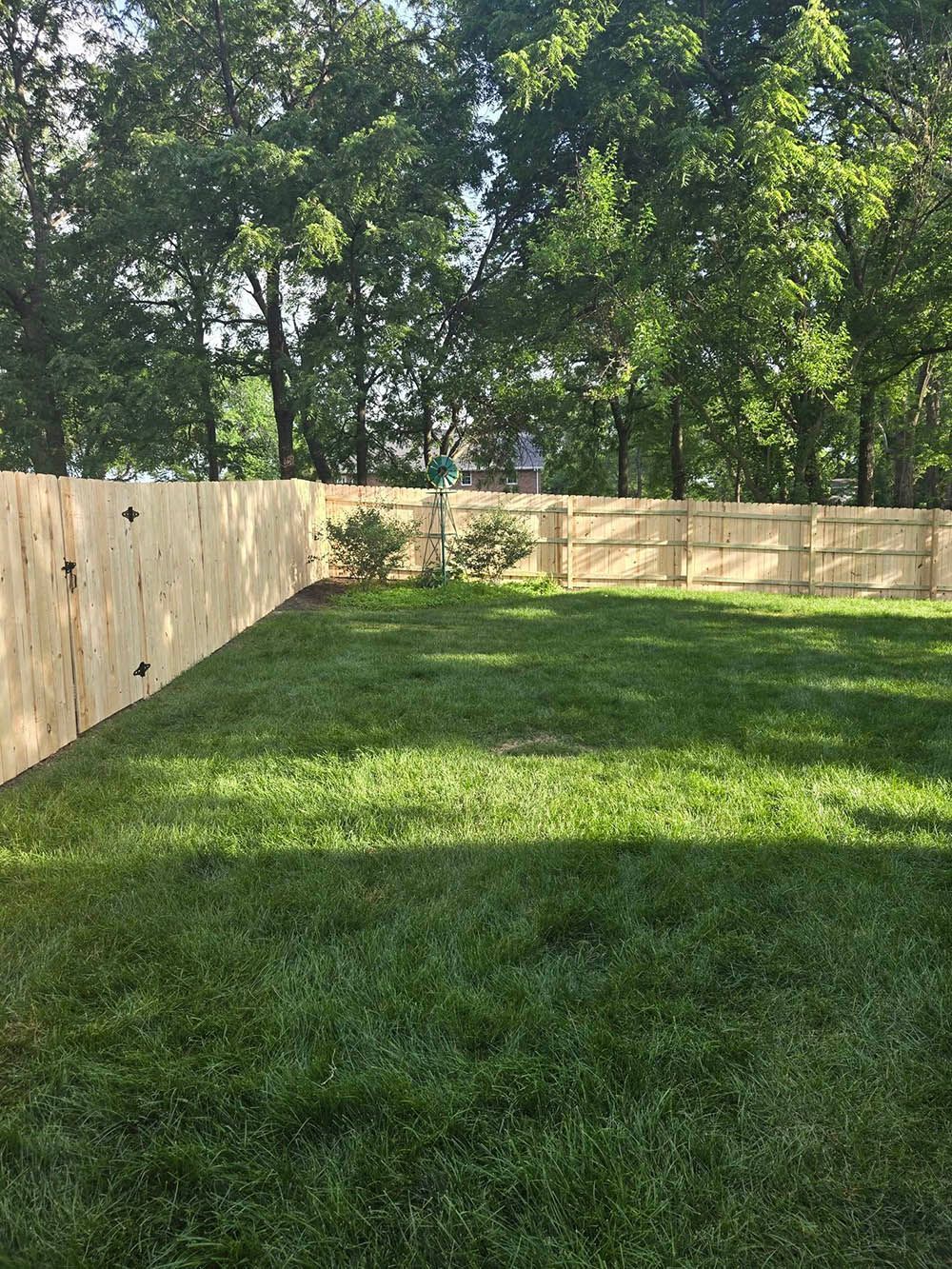 A wooden fence surrounds a lush green yard with trees in the background.