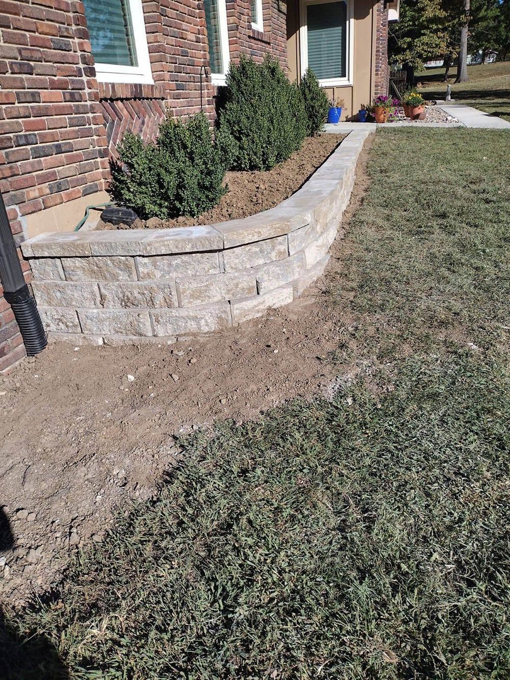 A brick wall is being built in front of a brick house.