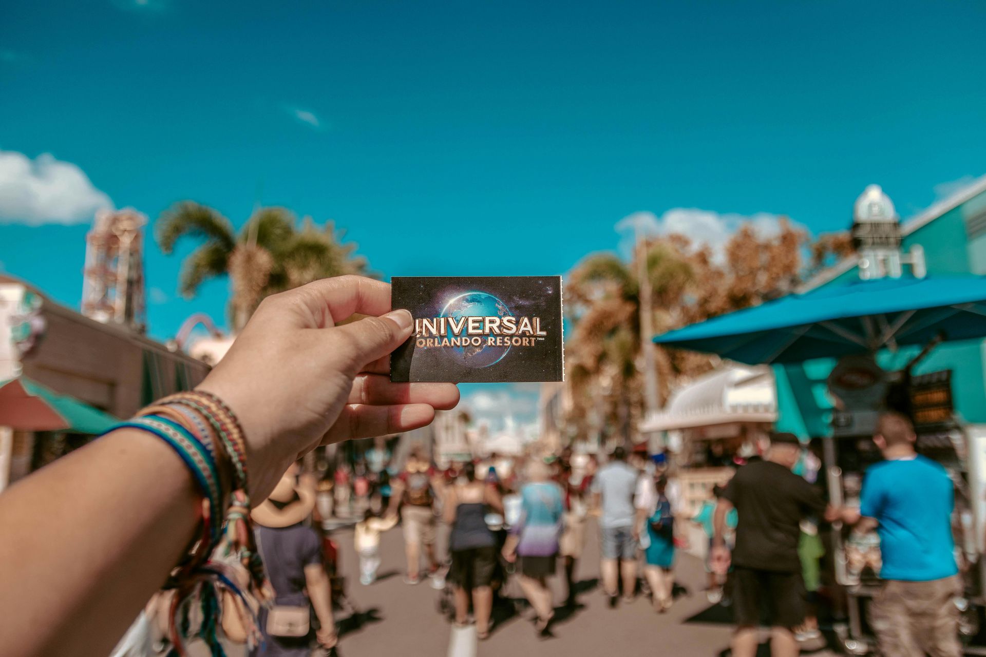 Person holds a Universal Orlando Resort card in front of a crowded street under a blue sky.