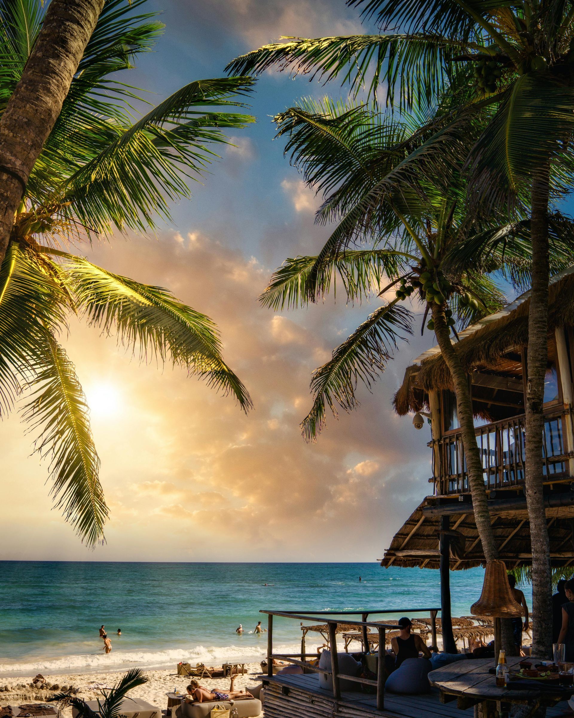 Red hammock strung between two palm trees on a beach, with ocean in the background.