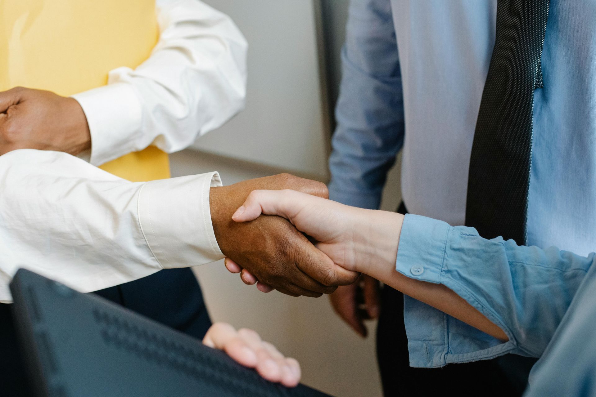 People shaking hands, close-up, indoors. One person wears a yellow top and the other a blue shirt.