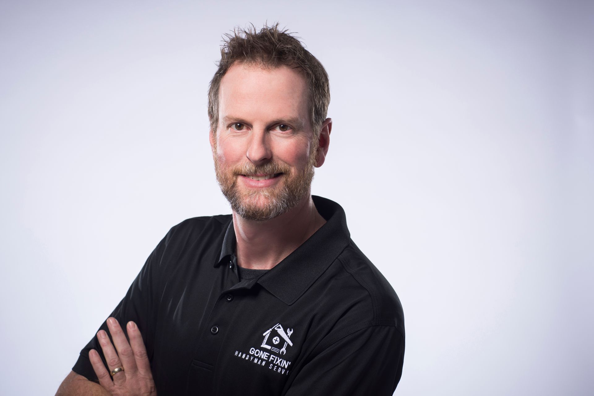 Man in black shirt with arms crossed, smiling, in front of a white background.