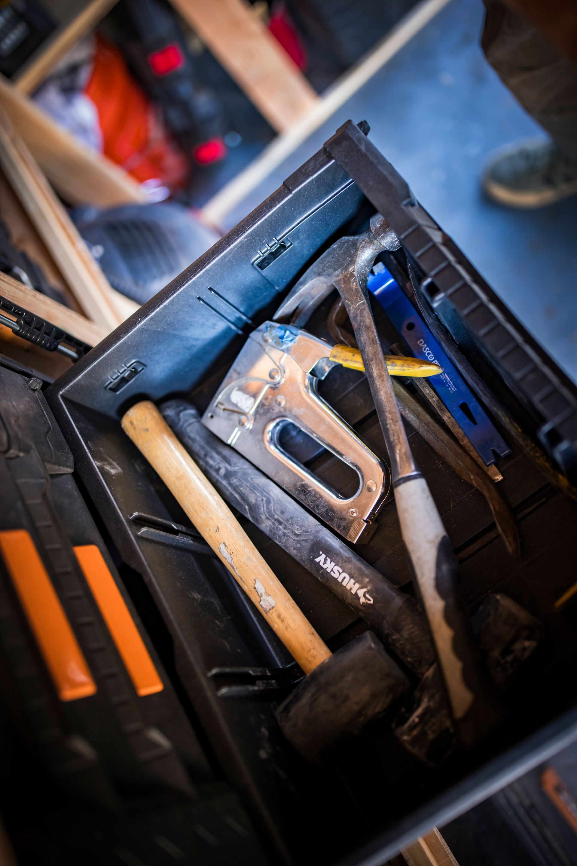 Black toolbox with hand tools: hammer, staple gun, crowbar, and pry bar.