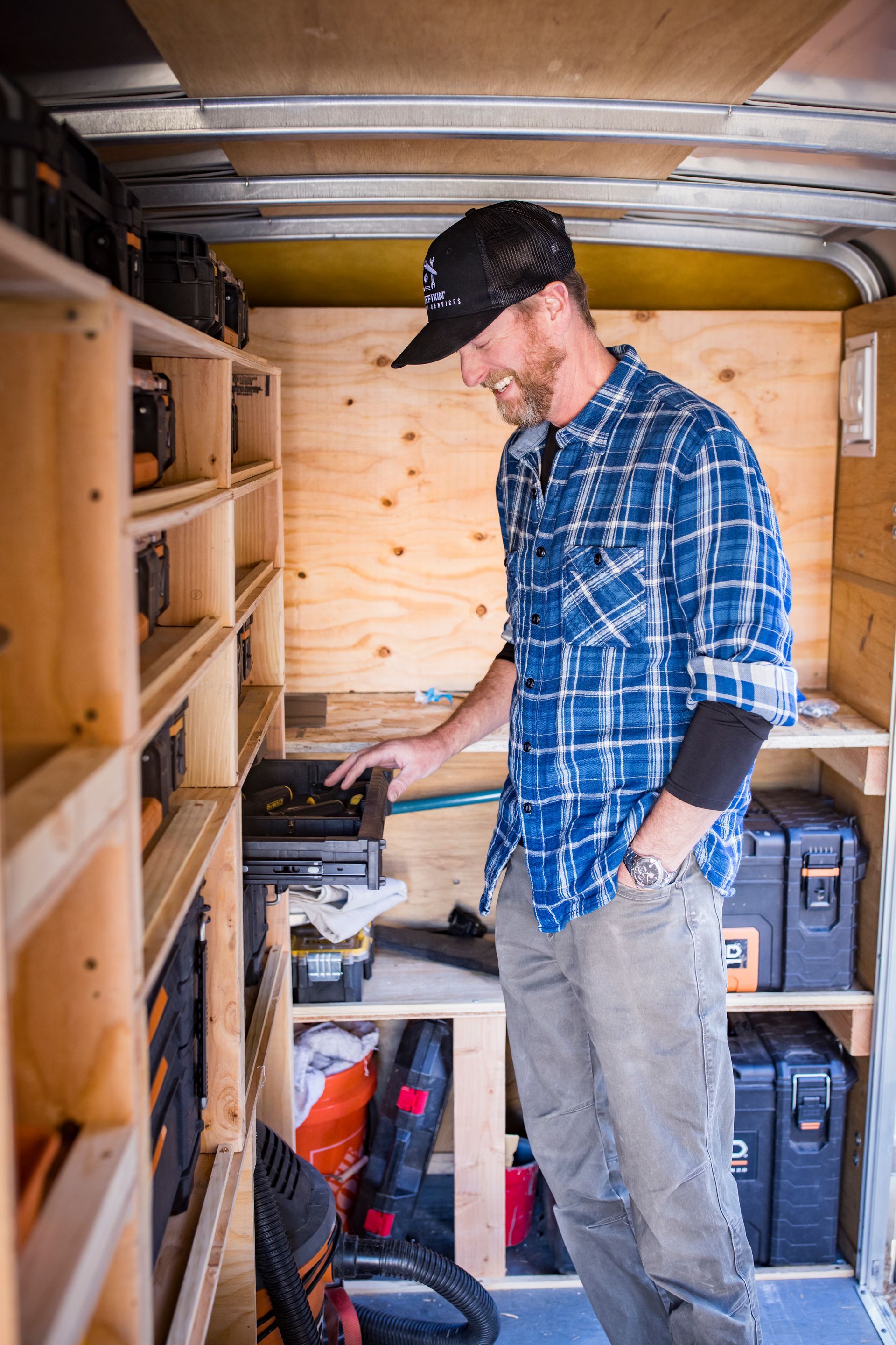 Man in plaid shirt inside a tool trailer, looking at a toolbox, surrounded by shelves of tools.