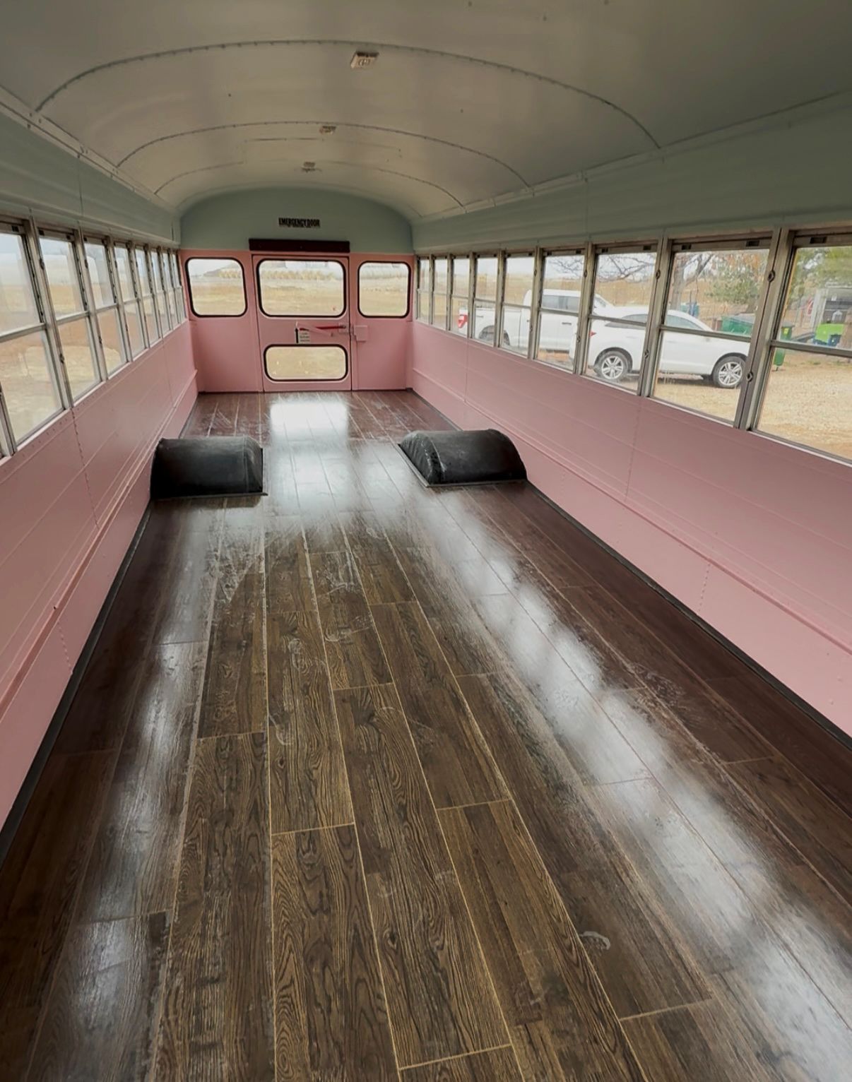 Interior of a school bus converted with wood flooring, pink walls, and large windows.
