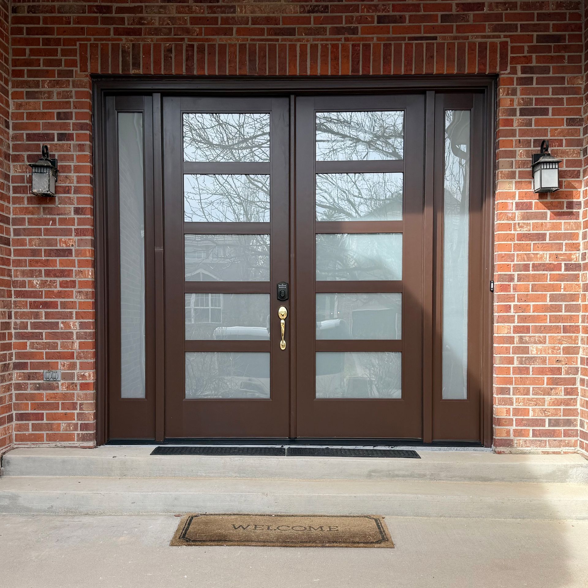 Brown double doors with glass panels and sidelights on a brick facade.