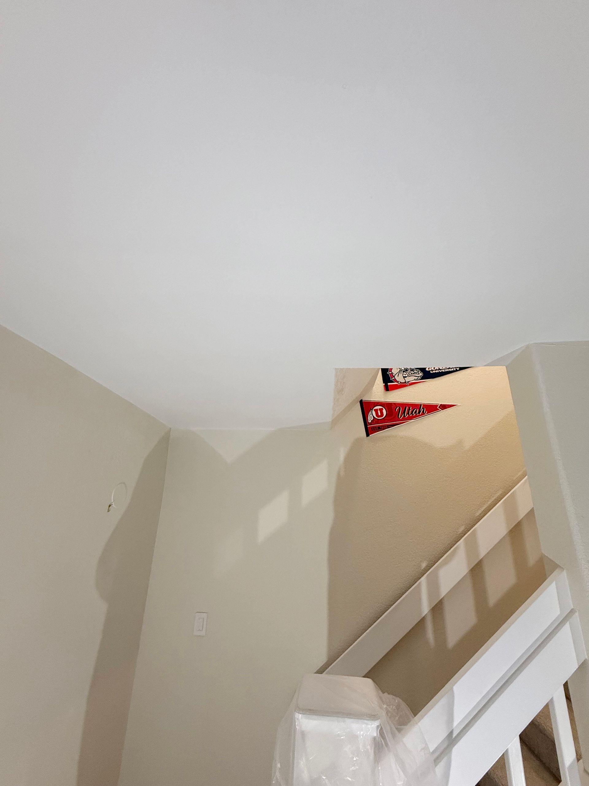 A staircase with white railings, beige walls, and red and white sports pennants hanging on the upper wall.