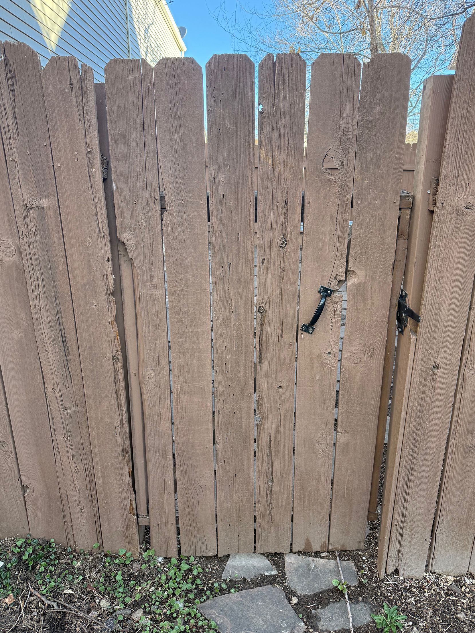 A weathered wooden privacy gate in an outdoor setting with a simple black latch.