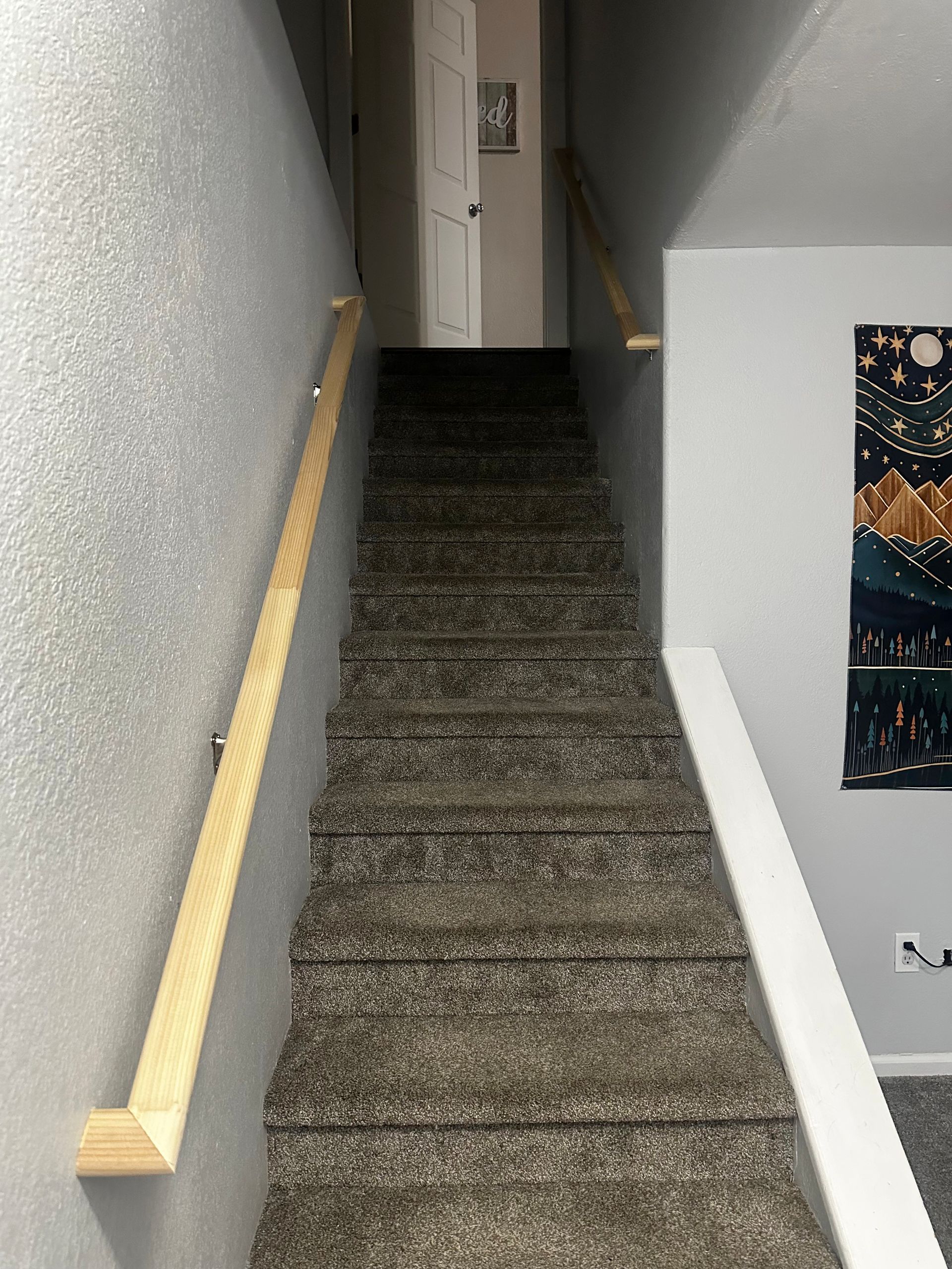 Staircase with carpet and wooden handrails leading up towards a white door. A tapestry hangs on the wall.