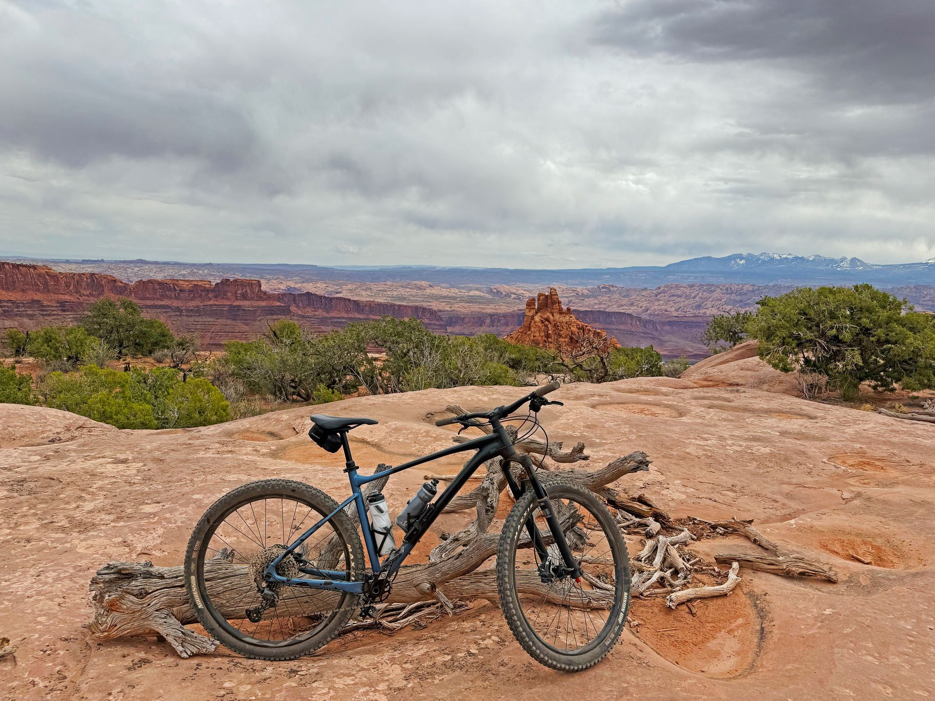 Mountain bike parked on red rock overlooking a vast desert landscape under a cloudy sky.