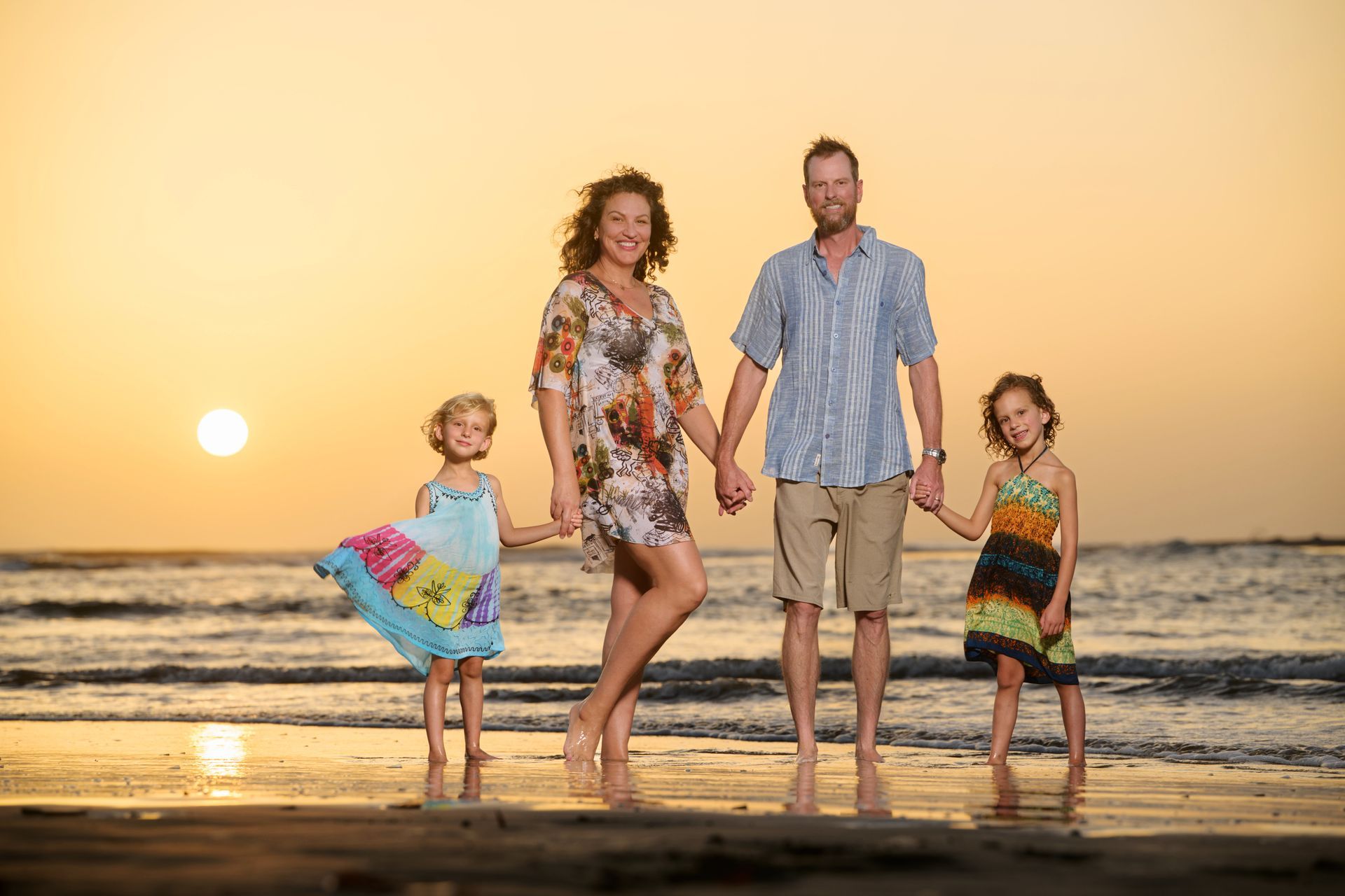 Family holding hands on beach at sunset.