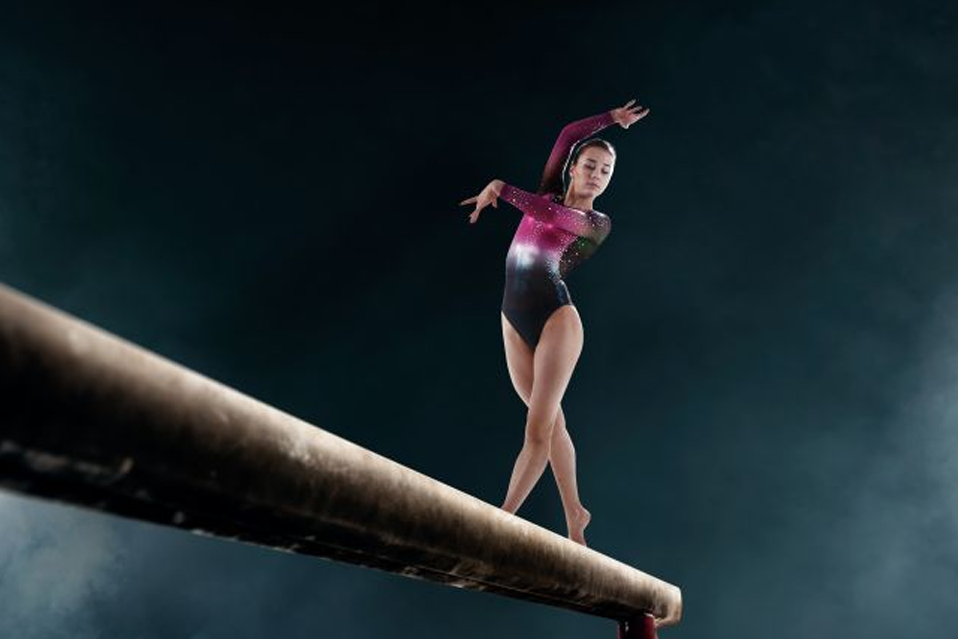 A young girl is sitting on a balance beam in a gym.